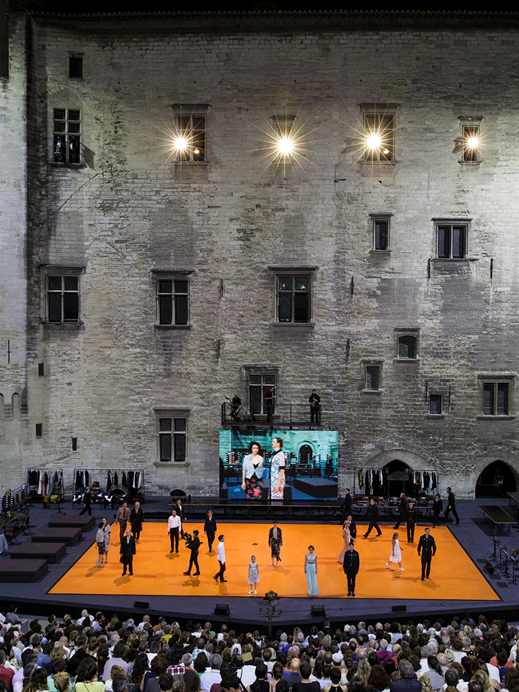 Image of a stage with actors performing, an audience in front and an ancient building at the back © Christophe Raynaud de Lage