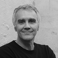 A black and white headshot photo of Italian theatre director Marco Martinelli