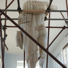 Photograph of an ancient Greek statue, without a head, surrounded by scaffolding