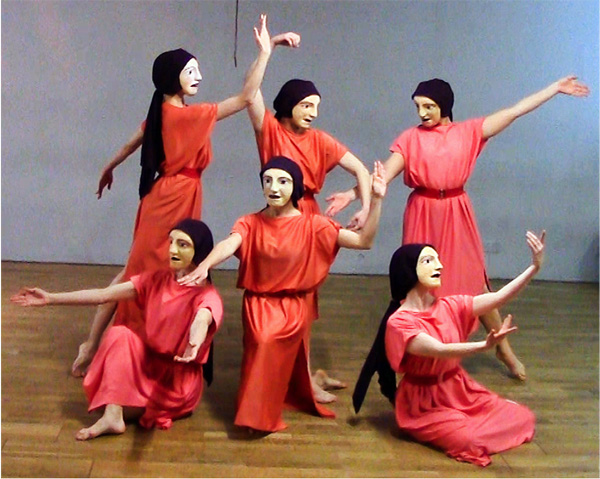 Six masked dancers in red robes perform a dance