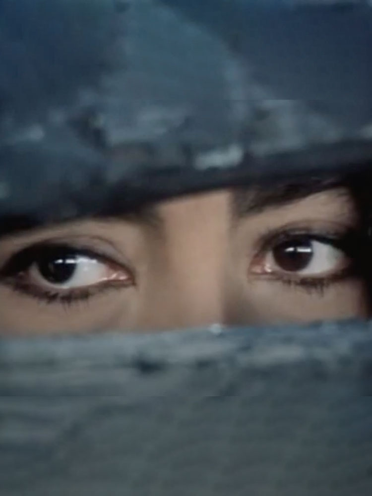 Film still showing close up of a pair of a woman's eyes looking out from within a wooden cage