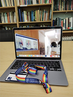 A photograph of a University of Oxford lanyard on top of an open laptop on a desk in a library