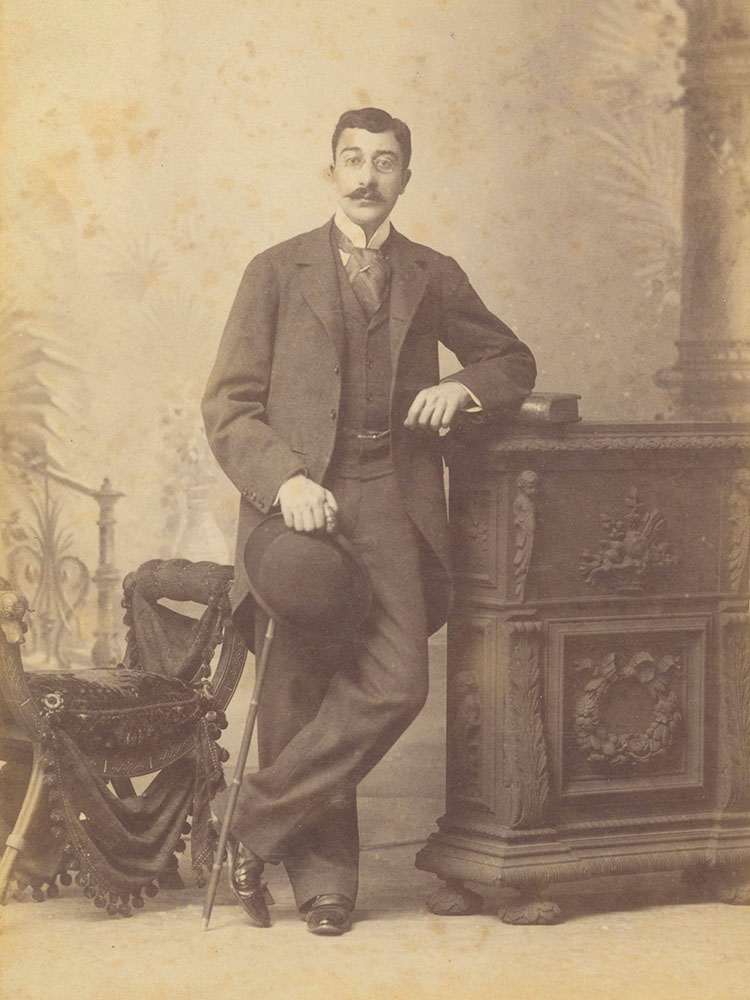 Image of writer Constantine Cavafy, full body picture of Cavafy leaning on a piece of furniture