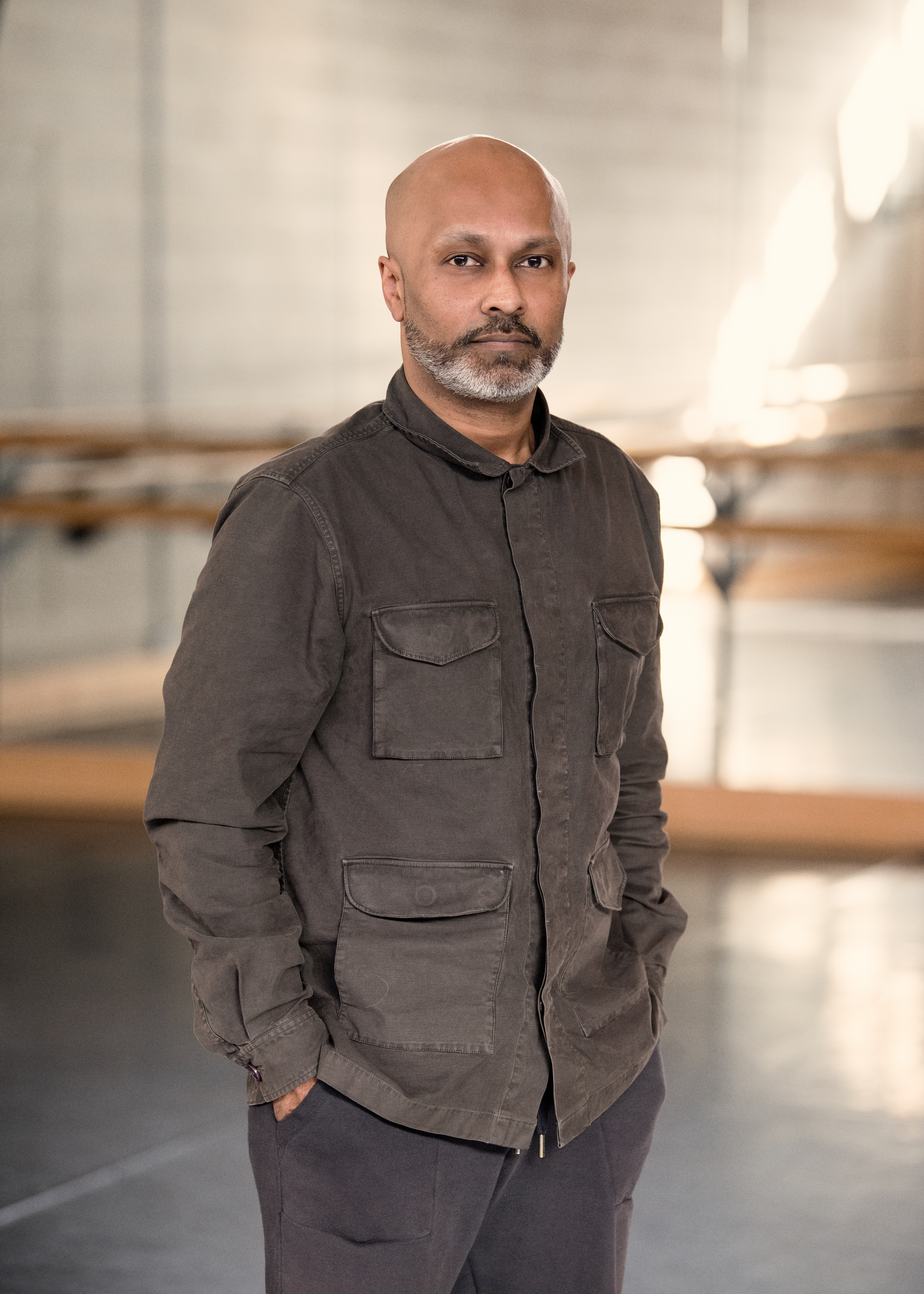 Photograph of Akram Khan in a dance studio, looking at the camera with his hands in his pockets
